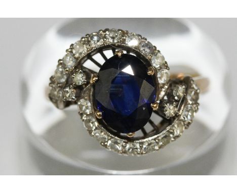 A sapphire and diamond ring, the oval cut stone within two scrolls of ten eight cut diamonds in 14ct gold