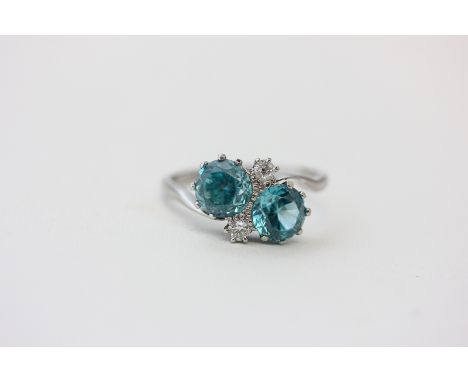 A blue zircon crossover ring claw set with two brilliant cut diamonds in 18ct white gold