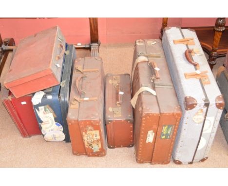 Seven vintage suitcases, some with travel labels and shipping labels.