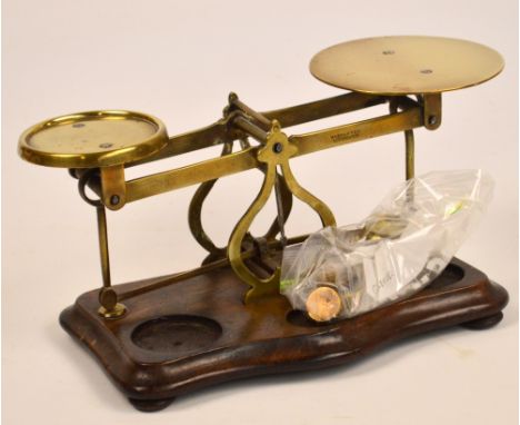 A set of brass postal scales mounted on shaped oak plinth, sold with five circular stacking weights.