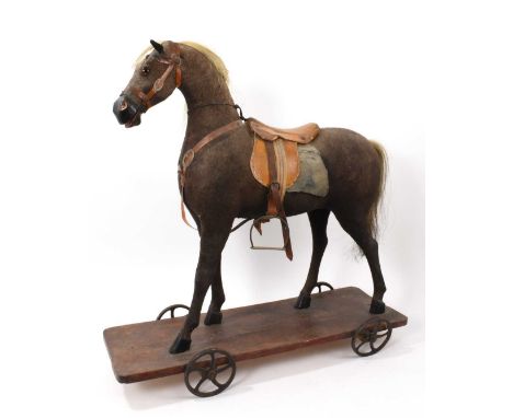 Late 19th / early 20th century child's pull along horse, with leather saddle, raised on platform with metal wheels, the platf