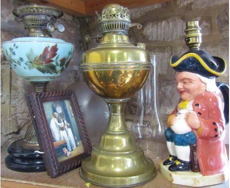 An oil lamp with a blue floral font with an etched glass shade, a brass base of an oil lamp, a Toby Jug style table lamp and 