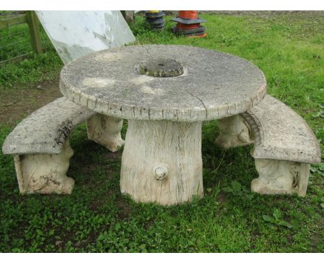 A novel weathered composition stone garden table with simulated rough hewn circular wooden top raised on a heavy simulated tr