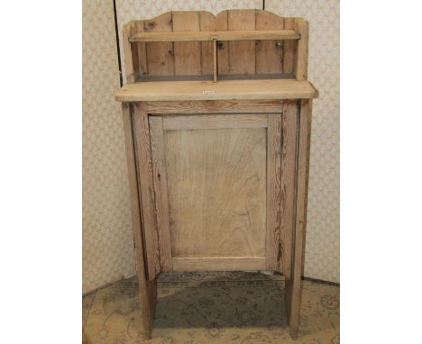 A small rustic stripped pine side cupboard enclosed by a rectangular panelled door beneath a raised fixed open shelf, 57 cm w