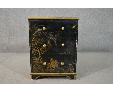 A circa 1920s Chinese style black lacquered bedside chest, painted and gilded with landscapes and flowers, the three long dra