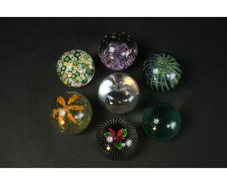 A collection of seven art glass paperweights, including a Caithness black 'Flower in the Rain' design paperweight and a cane 
