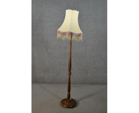 A circa 1920s fruitwood standard lamp, with a turned stem and a circular base, the cream shade hung with beaded tassels. H.18