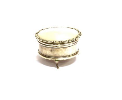 A SILVER SMALL ROUND TRINKET BOX on three pad feet, the hinged lid with a shaped 'C' scroll border and enclosing a pale blue 