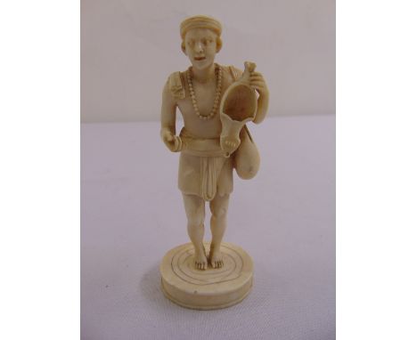 A 19th century ivory figurine of a man carrying a bag and oil lamp on raised circular base