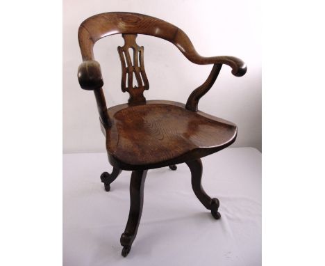 An Edwardian oak captains swivel desk chair with a cut out seat on four sweeping legs on original ceramic castors