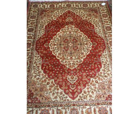 A Persian style Kum red ground carpet, having quatrefoil medallion to centre on a floral ground, multi-bordered and fringed. 