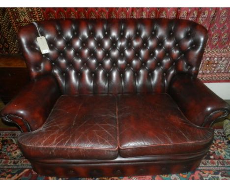 A Chesterfield style two seater sofa, upholstered in red burgundy, raised on casters.