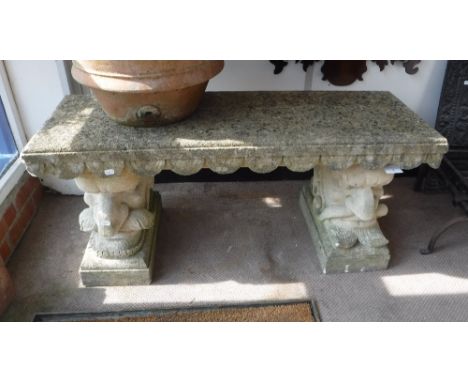 A RECONSTITUTED STONE BENCH, supported by grotesque faces, 18" high x 42" wide x 15" deep