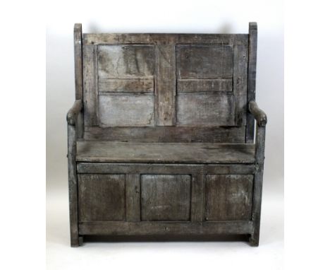 An oak panel back settle, 18th century and later, with four fielded panels to the back, above a fixed seat and open arms over