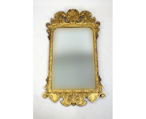 A George III carved gilt wood wall mirror, the bevelled rectangular plate with re-entrant top corners below a shell centred a