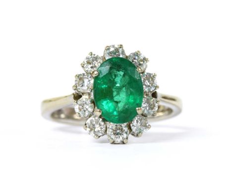 An 18ct white gold emerald and diamond oval cluster ring, with a central oval mixed cut emerald, estimated as approximately 1