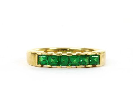 A gold six stone tsavorite garnet ring, with a row of square step cut tsavorite garnets, claw set, to a slightly tapered ligh