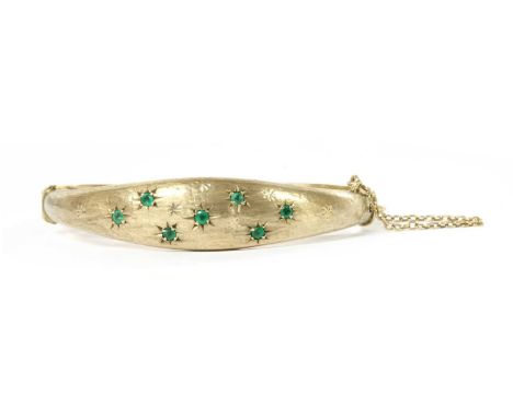 A 9ct gold emerald hinged bangle, by Smith &amp; Pepper, with round mixed cut emeralds star set to the textured tapered top h