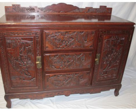 A Chinese carved sideboard with three central drawers flanked by cupboards enclosed by two panelled doors, decorated all-over