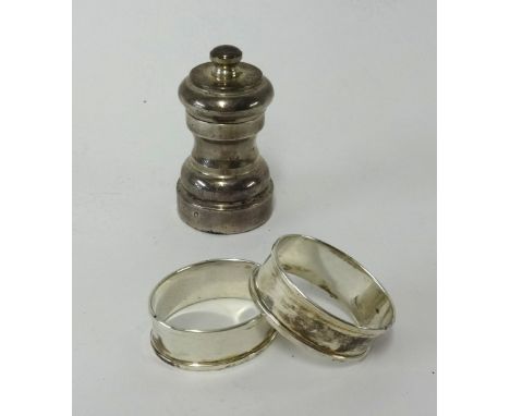 A pair of silver napkin rings and a silver pepper grinder.