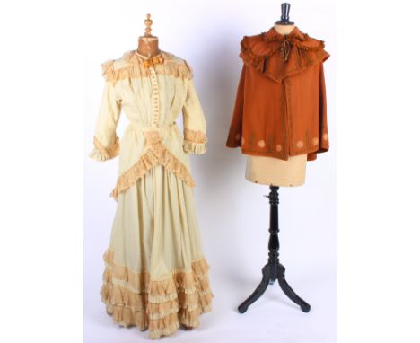 Five items of 19th century ladies costume, comprising: a black grosgrain cape, a fine wool cream outfit with a lace trimmed c