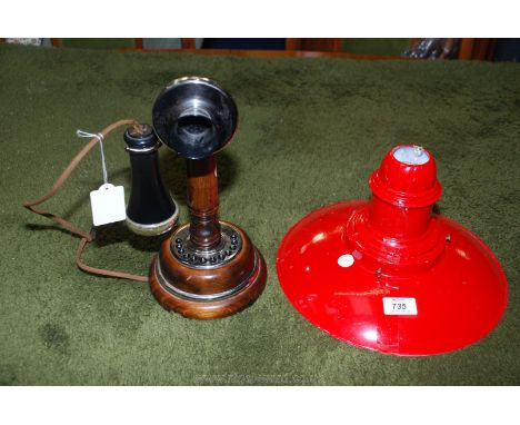 A candlestick style telephone and red metal lamp shade.