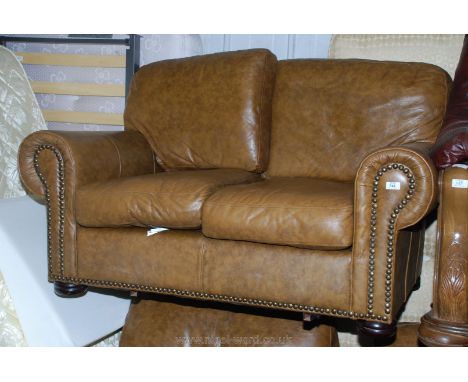 A tan twin sofa and two matching armchairs in leather with brass stud detail.