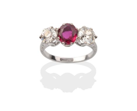 A Ruby and Diamond Three Stone Ring, an oval cut ruby between old cut diamonds in white claw settings, to scroll motif should