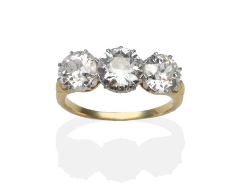 A Diamond Three Stone Ring, graduated old cut diamonds in white claw settings, to yellow scroll shoulders on a plain polished