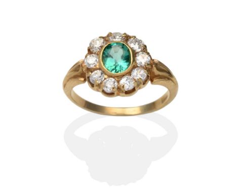 An Emerald and Diamond Cluster Ring, an oval cut emerald in a yellow rubbed over setting, within a border of old cut diamonds