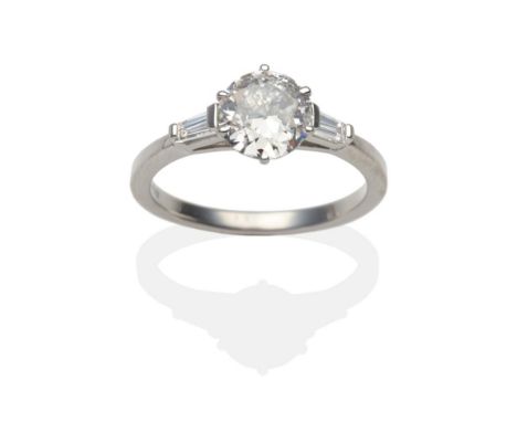 A Platinum Diamond Solitaire Ring, an old cut diamond in a claw setting between tapered baguette cut diamonds, on a plain pol