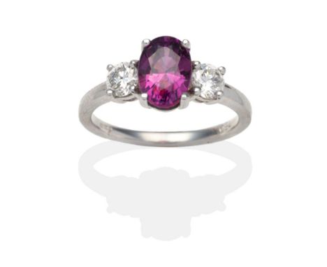 An 18 Carat White Gold Purple Sapphire and Diamond Three Stone Ring, an oval cut purple sapphire between two round brilliant 