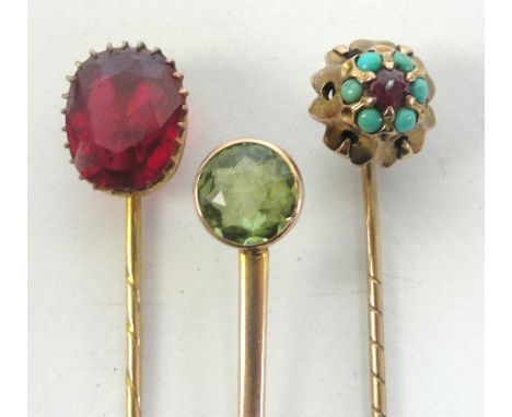 A yellow metal stick pin set with large ruby terminal, length 6.25cm, a 9ct gold stick pin set with a green peridot, length 6