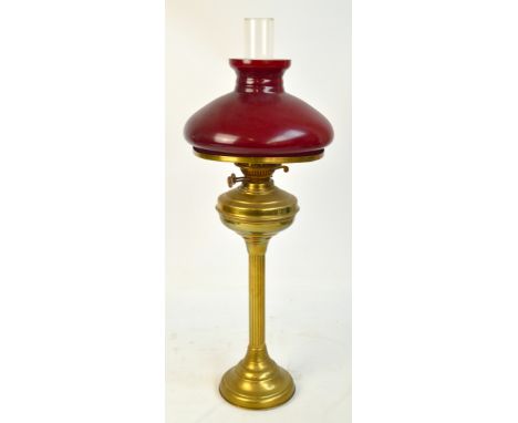 A brass oil lamp with white and red glass shade, on fluted column to spreading circular foot, height 65cm.