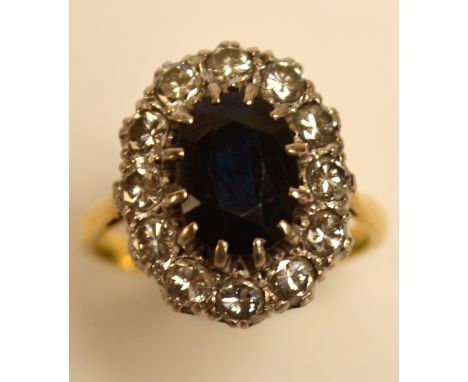 An 18ct gold diamond and sapphire ring, the central oval sapphire set within a border of diamonds in pierced scroll mounts, s