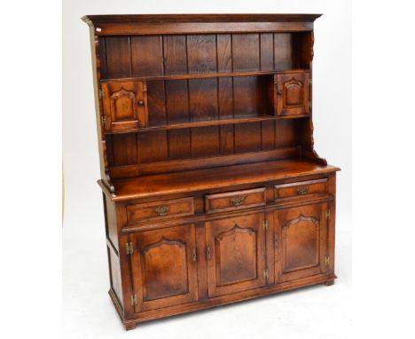 A reproduction oak dresser, the boarded plate rack with twin fielded panel doors above a base of three frieze drawers above t