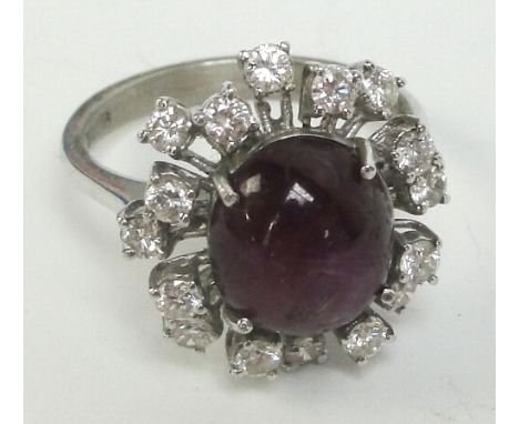 An 18ct white gold diamond and star ruby ring, the central oval cabochon ruby within a border of stepped diamonds in scrollin