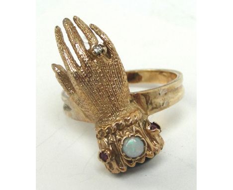 A 9ct gold ring unusually set with a hand, with garnet cabochon to the wrist, band set with opal and two small rubies and tin