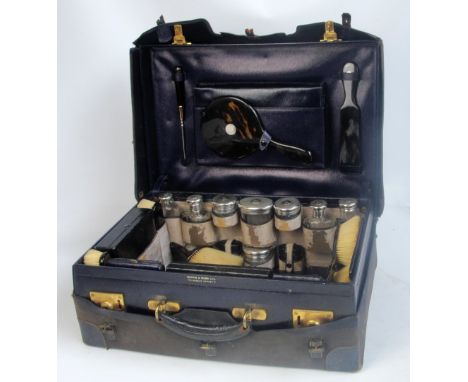 An early 20th century leather vanity case housing five George V hallmarked silver topped dressing jars, a pair of scent bottl