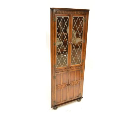 A reproduction oak freestanding corner cupboard with leaded glazed upper section and panel door beneath.