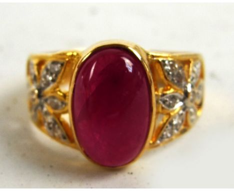 A yellow metal ruby and diamond ring, the central oval cabochon ruby flanked by diamond set flower heads in a pierced mount, 