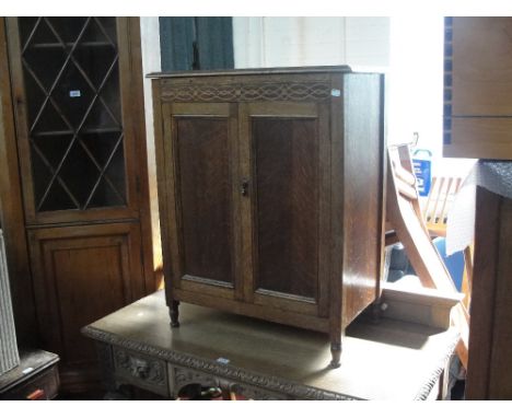 An early 20th century oak record cabinet with double hinged doors enclosing a sectioned interior with one shelf, with carved 