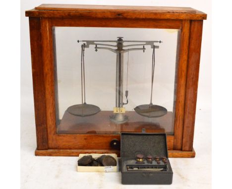 A set of oak cased chemist balance scales with glazed sides and a quantity of various weights, cabinet width 47cm.