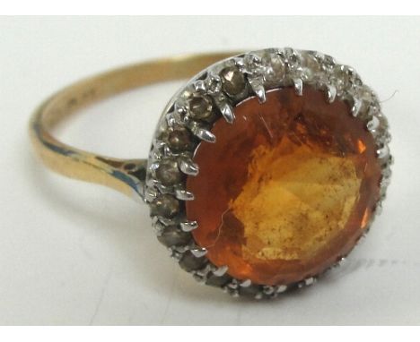An 18ct gold orange topaz and diamond ring, the central circular topaz within a border of diamonds in a scrolled setting, siz