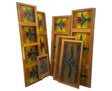 Collection of leaded stained glass window panes in mahogany frames, depicting central stylised tulip flower in green and red 
