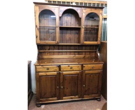 A 1.3m Ducal stained pine two part dresser with central open shelves and flanking glazed panel doors over a base with three f