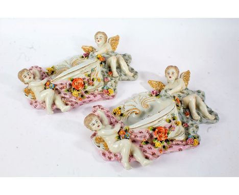 Pair of Continental porcelain wall pockets, each centred with a scallop shaped dish, flanked by a cherub either side and flow