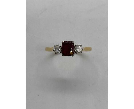 An 18ct yellow gold ruby and diamond three stone ring, the central cushion cut ruby flanked by twin claw set round brilliant 