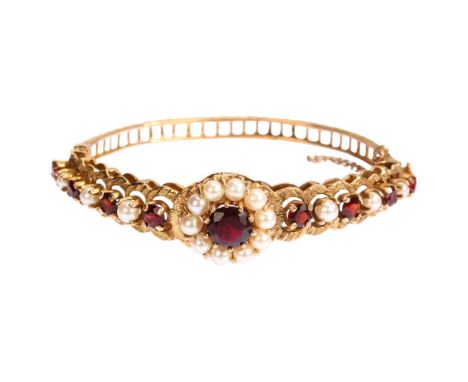 A mid-20th century 9ct gold garnet and pearl cluster hinge bangle, with central flowerhead cluster flanked by graduated row o
