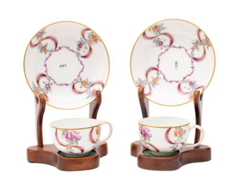 A pair of Zurich teacups and saucers, each painted with floral sprays amongst puce ribbons around a central foliate cartouche